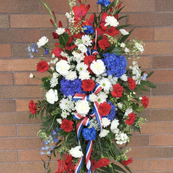 Standing floral wreath with red, white, and blue flowers on a ribboned easel