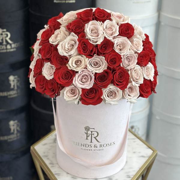 Red and blush roses arranged in a round pink hat box
