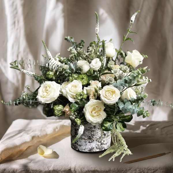 White roses and greenery arranged in a black-and-white vase
