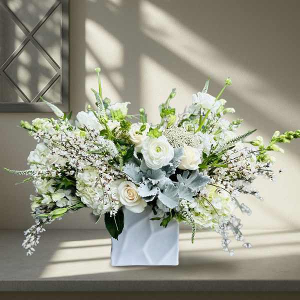 White floral arrangement in a white square vase with silver foliage