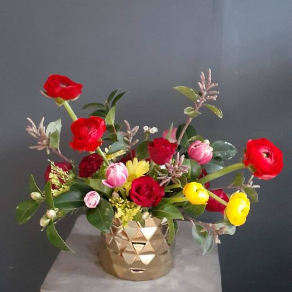 Mixed bouquet of red, pink, and yellow flowers in a gold vase