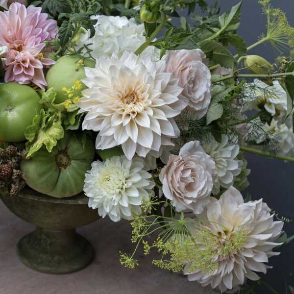 Arrangement of white and blush flowers with green fruit in a pedestal bowl