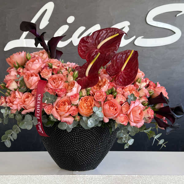 Pink and coral roses in a black vase with dark red anthuriums