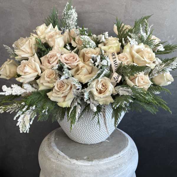 Cream roses in a white textured vase with evergreen accents