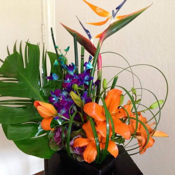 Tropical arrangement with orange lilies and purple orchids in a black container