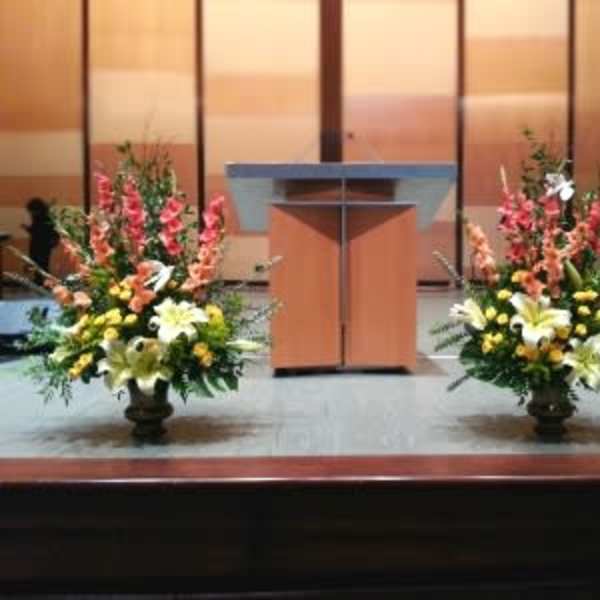 Two large floral arrangements flank a podium on a stage.