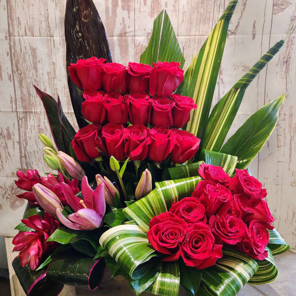 Red roses and pink lilies arranged in a wooden box with striped leaves
