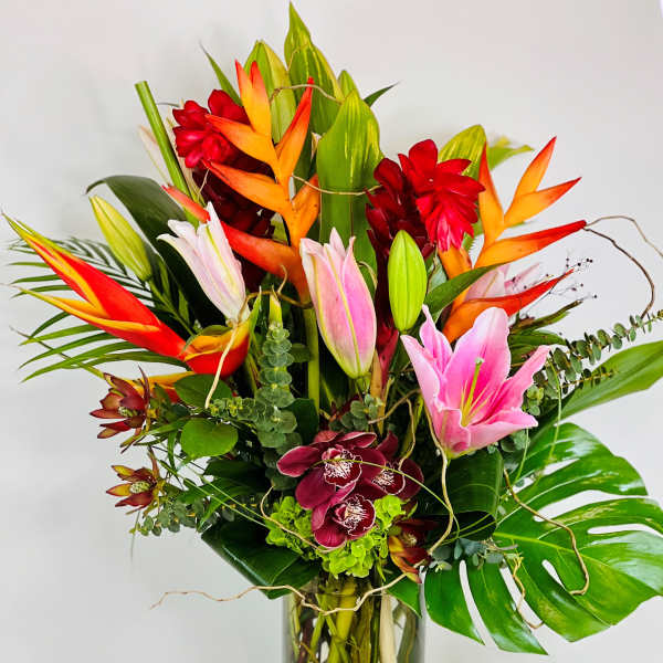 Tropical bouquet with pink lilies, orchids, and orange heliconia in a glass vase