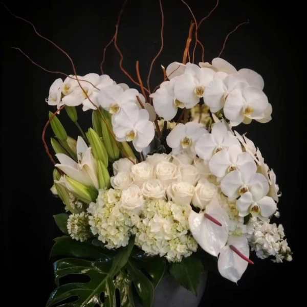 White orchids and roses arranged in a dark vase with tropical leaves