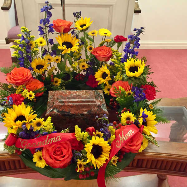 Colorful floral wreath around a memorial urn with red ribbons