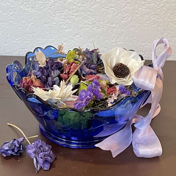 Dried flower arrangement in a blue glass bowl with a pink ribbon