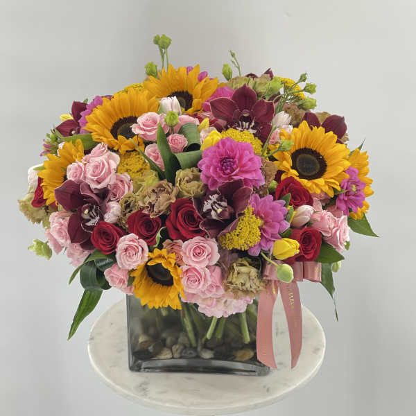 Mixed bouquet with sunflowers, roses, and orchids in a square glass vase