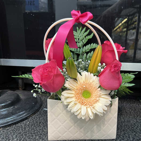 Pink roses and a cream gerbera daisy in a gift bag with a ribbon handle