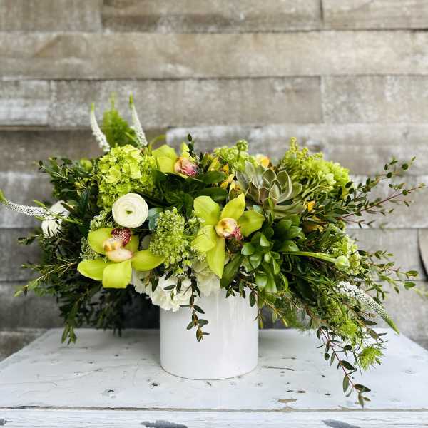 Green floral arrangement in a white vase with orchids and succulents