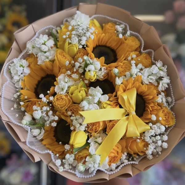 Bouquet of sunflowers, yellow roses, and white filler flowers with a yellow ribbon