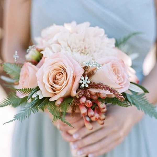 Hand-tied bouquet of peach roses and pale dahlias with berries held by a person in a light dress