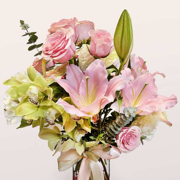 Pink roses and lilies arranged in a glass vase with a ribbon