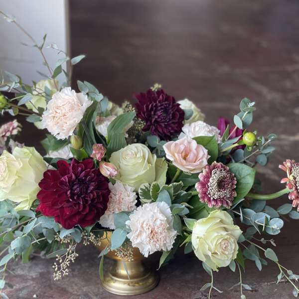 Low floral arrangement with roses, carnations, and dark dahlias in a gold vase