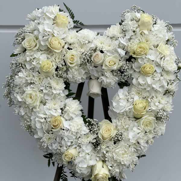 Heart-shaped white floral wreath with cream roses on a stand