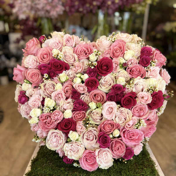 Heart-shaped arrangement of pink and white roses on a moss-covered base