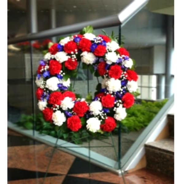 Patriotic wreath of red, white, and blue flowers displayed on a metal easel stand.