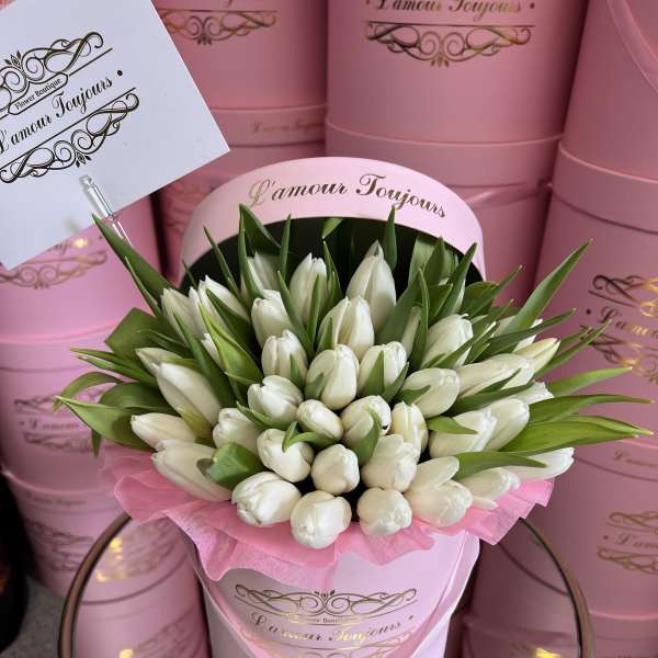 White tulips arranged in a pink hat box with green leaves