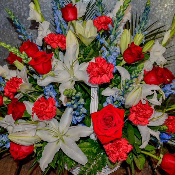 Red roses, white lilies, and blue flowers in a basket arrangement
