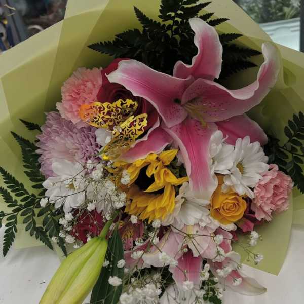 Bouquet of pink lilies, roses, daisies, and carnations wrapped in pale green paper