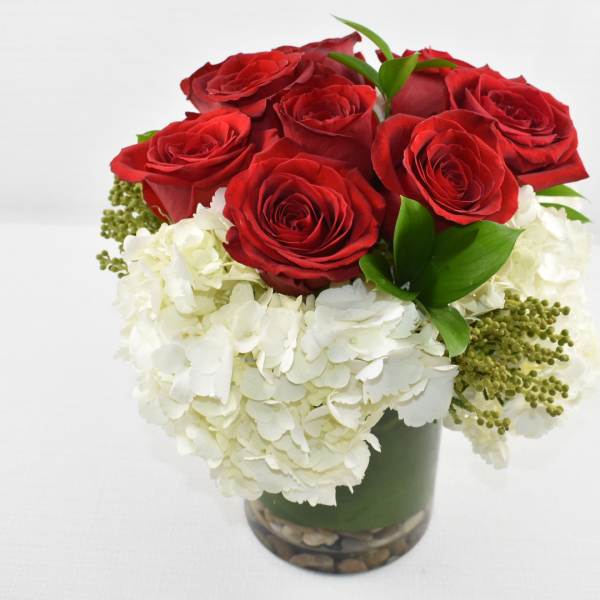 Compact arrangement of red roses and white hydrangeas in a glass cylinder vase