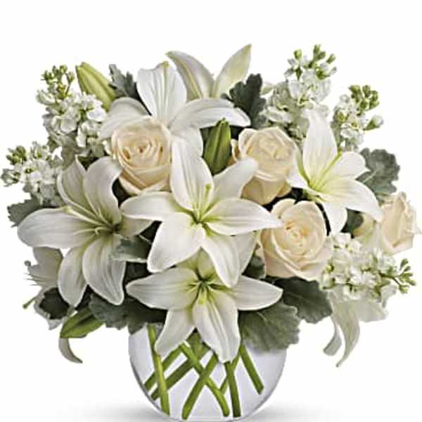 White lilies and cream roses arranged in a clear glass vase