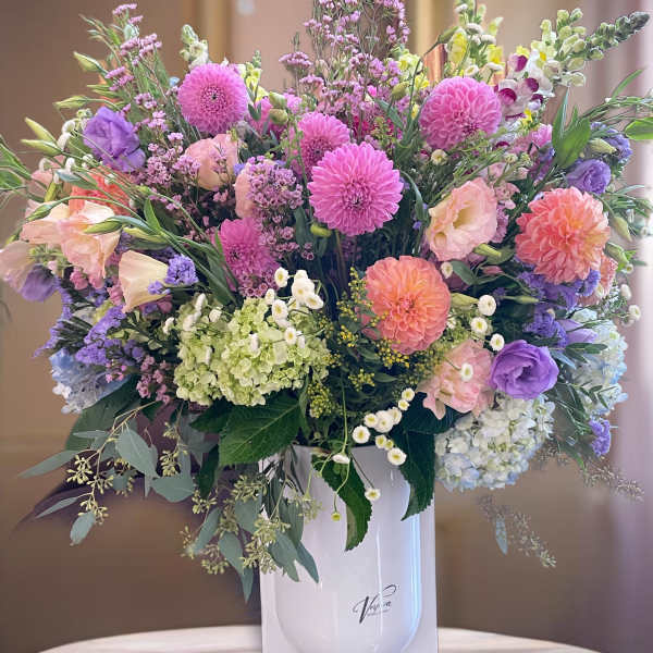 Large pastel bouquet in a white vase with pink, purple, peach, and green blooms