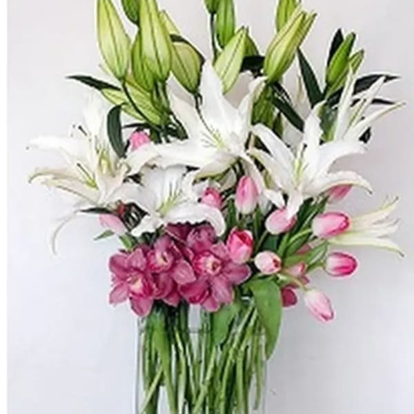 Tall bouquet of white lilies and pink orchids in a clear glass vase