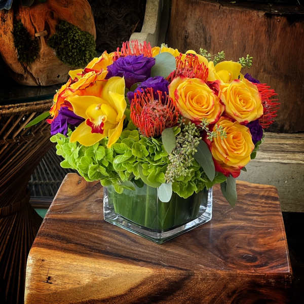 Bright bouquet of yellow roses, purple blooms, and orchids in a glass vase