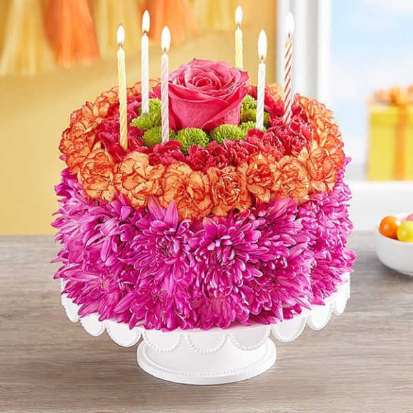 Flower cake with pink and orange blooms topped by a rose and candles