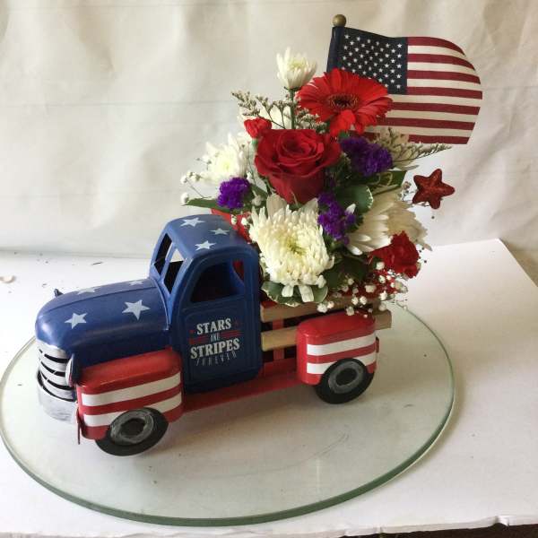 Floral arrangement in a patriotic truck-shaped container with an American flag topper