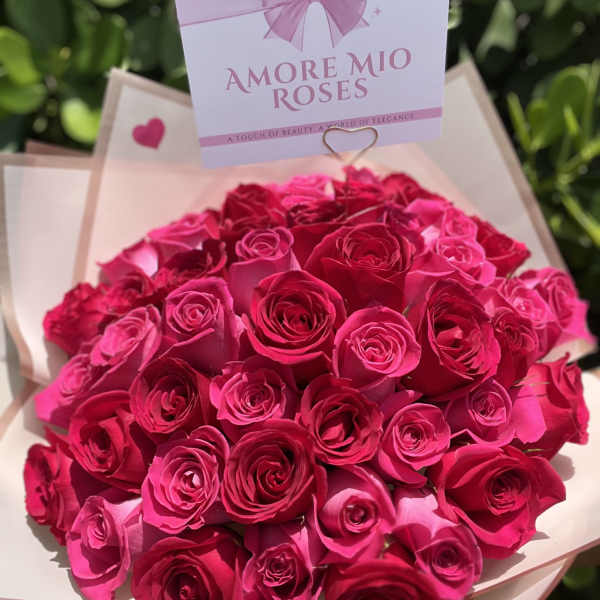 Bouquet of bright pink roses wrapped in pale paper with a gift card
