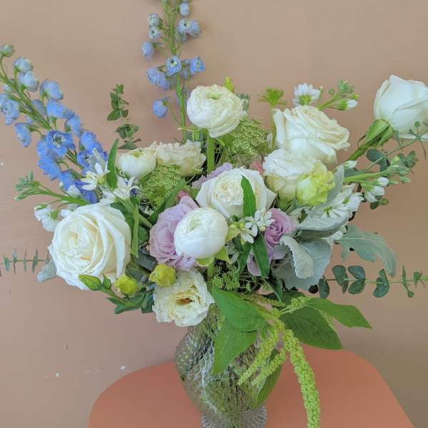 Mixed bouquet of white roses, pale blooms, and blue flowers in a glass vase