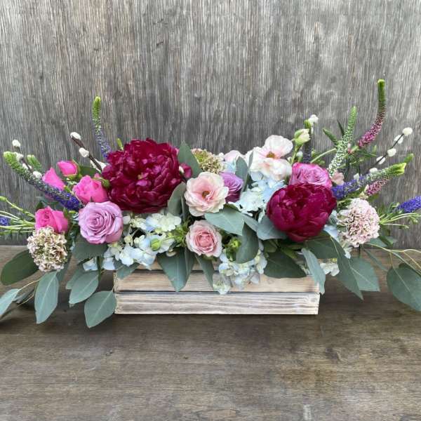 Low floral arrangement with pink and burgundy blooms in a wooden box