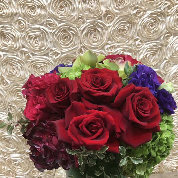 Bouquet of red roses with purple and green blooms in a glass vase