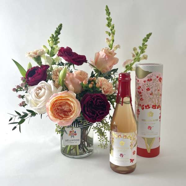 Bouquet of roses and snapdragons in a glass vase beside a bottle and gift box