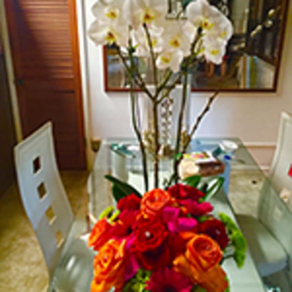 Tall white orchids with a bright cluster of red and orange roses in a clear vase on a glass table