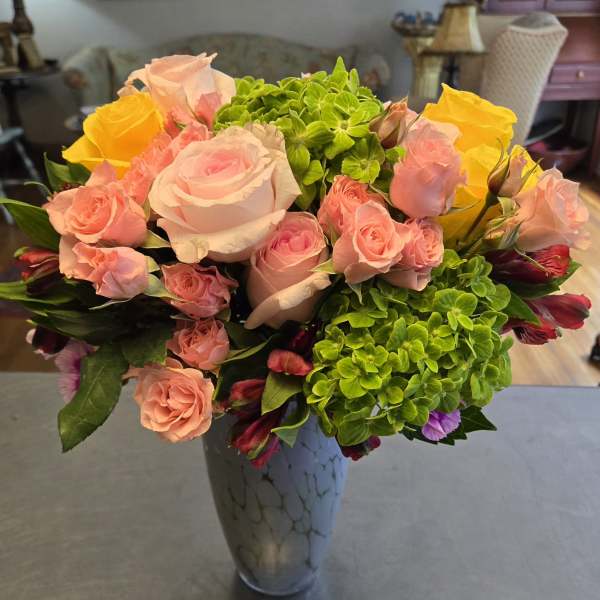 Pink and yellow roses with green hydrangeas in a tall vase