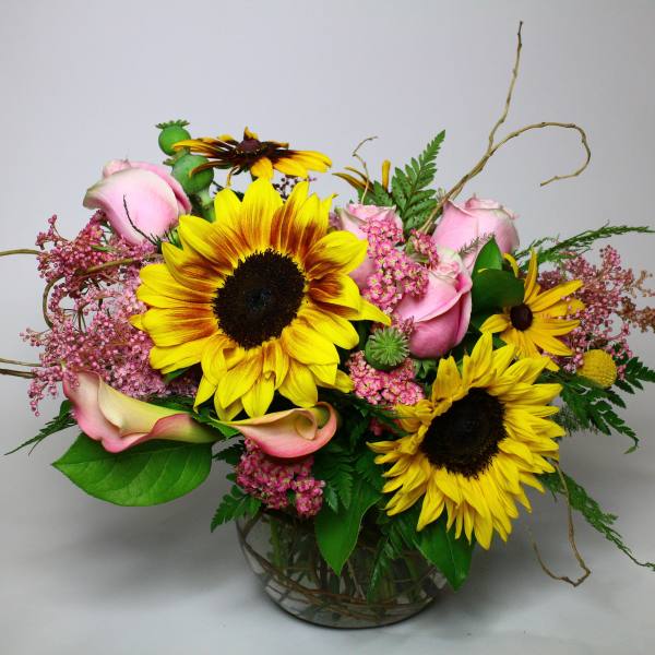 Bouquet of sunflowers, pink roses, and calla lilies in a glass vase