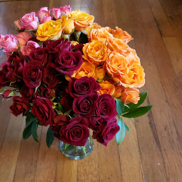 Bouquet of red, pink, orange, and yellow roses in a clear glass vase