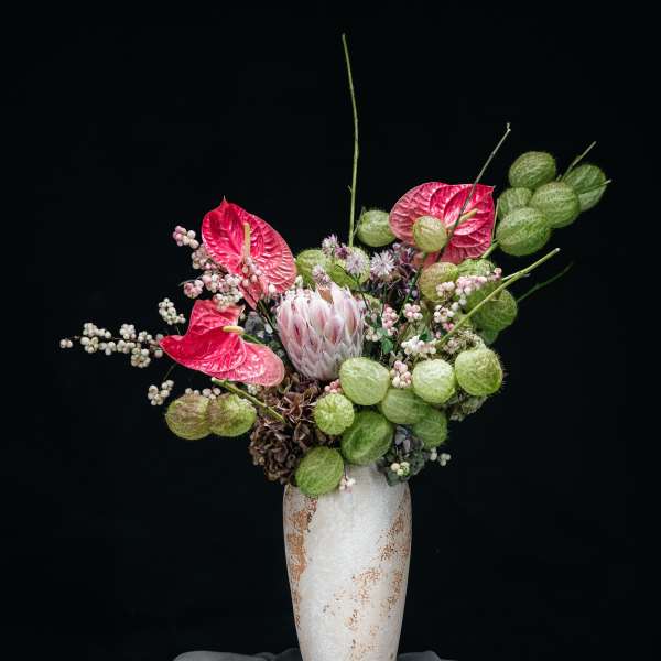 Pink anthuriums and pale flowers in a tall white vase