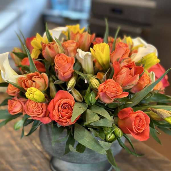 Orange roses and yellow tulips arranged in a metal vase