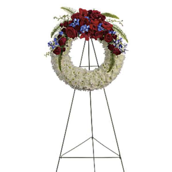 Standing funeral wreath with red and white flowers and blue accents on an easel