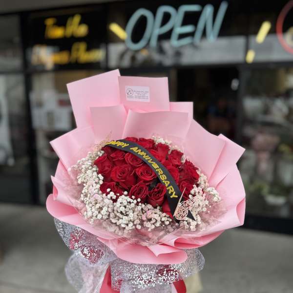Bouquet of red roses wrapped in pink paper with a Happy Anniversary ribbon