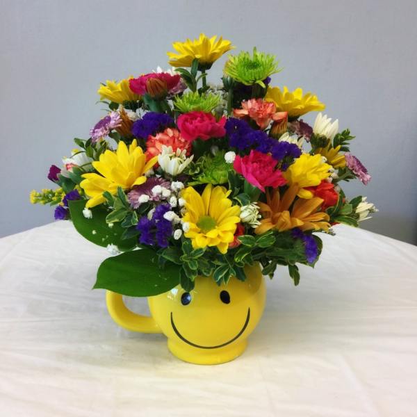 Colorful mixed flower arrangement in a yellow smiley-face mug