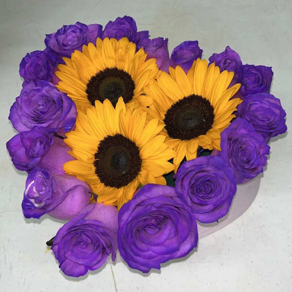 Low round arrangement of bright yellow sunflowers surrounded by vivid purple roses in a shallow container